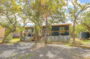 A rustic cabin with a wooden deck and a large window, surrounded by trees.