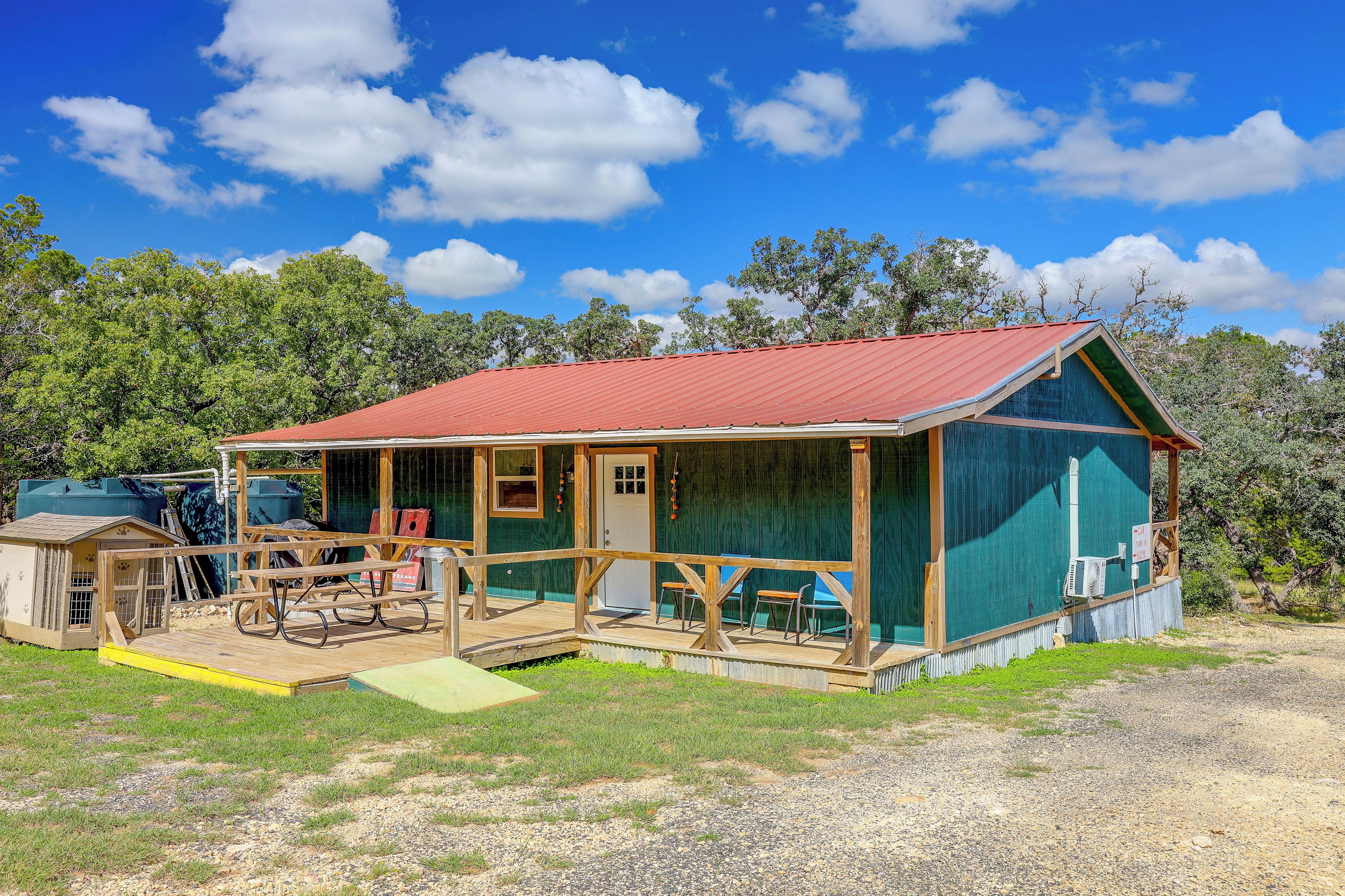 A rustic cabin with a red roof, wooden deck, and outdoor seating area.