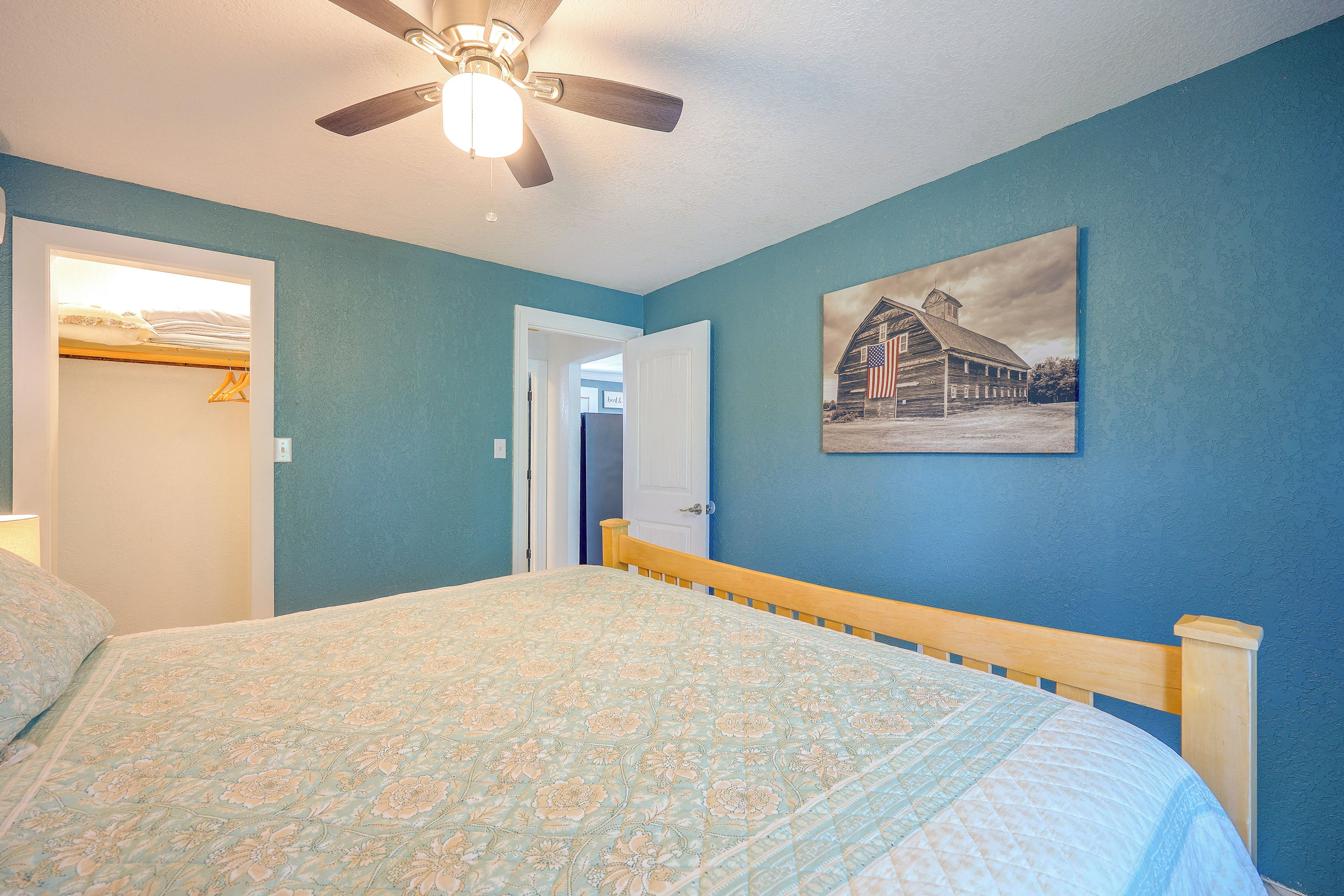 A bedroom with a bed, a ceiling fan, a door, and a wall-mounted picture.