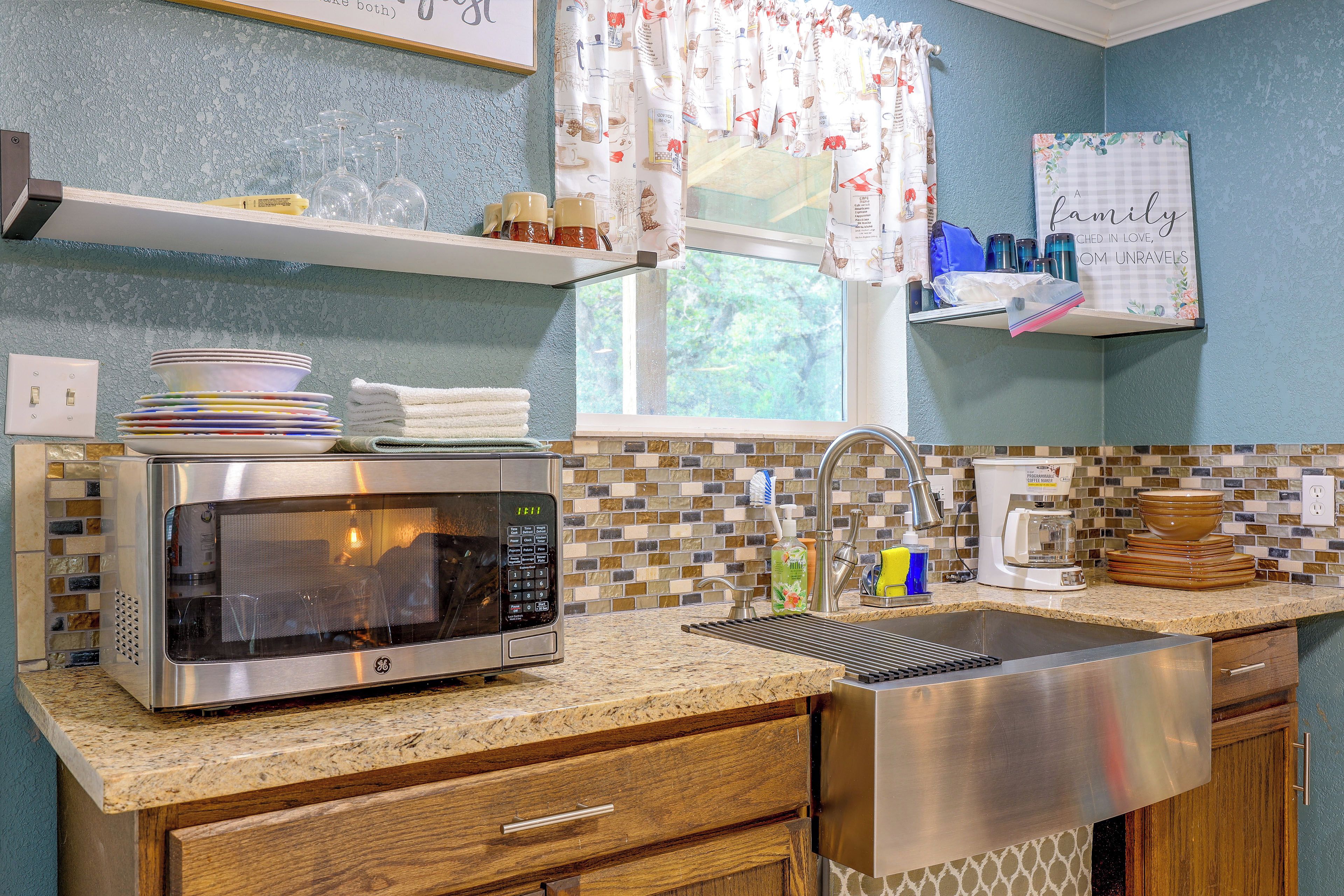 A kitchen with a microwave, coffee maker, sink, and a window with a view of greenery.