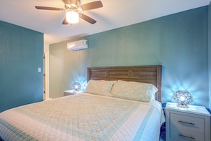 Un dormitorio con cama, mesitas de noche, ventilador de techo y unidad de aire acondicionado.