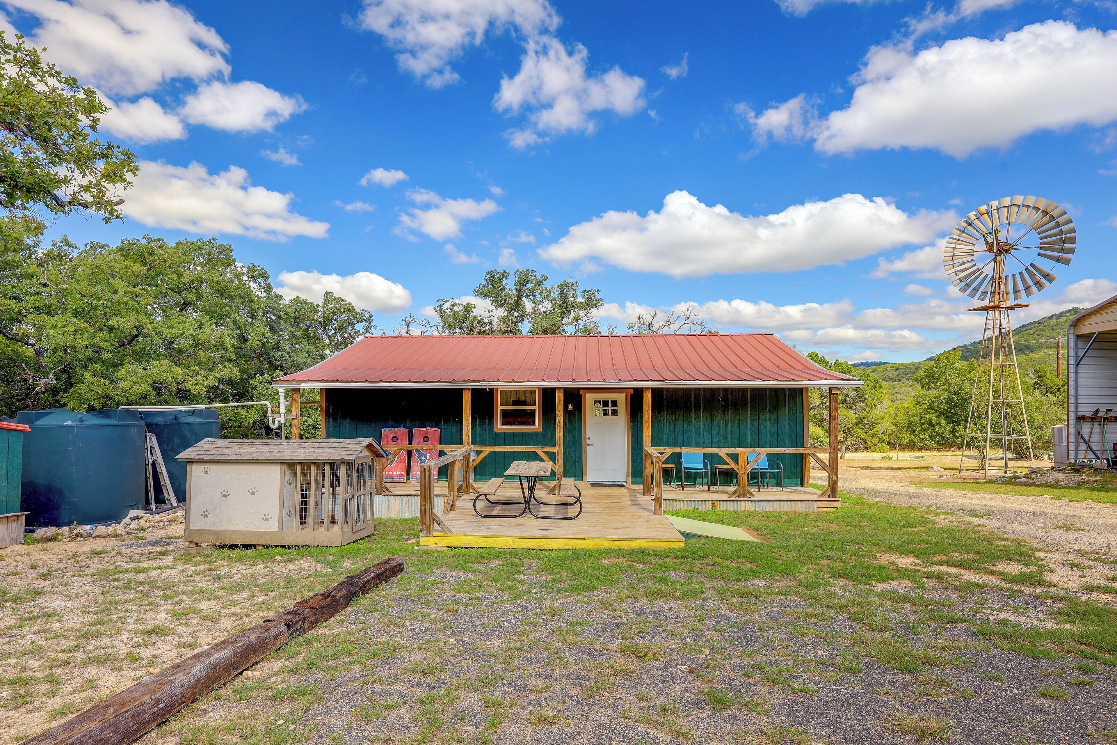A rustic cabin with a red roof, a wooden porch, and a windmill in the background.