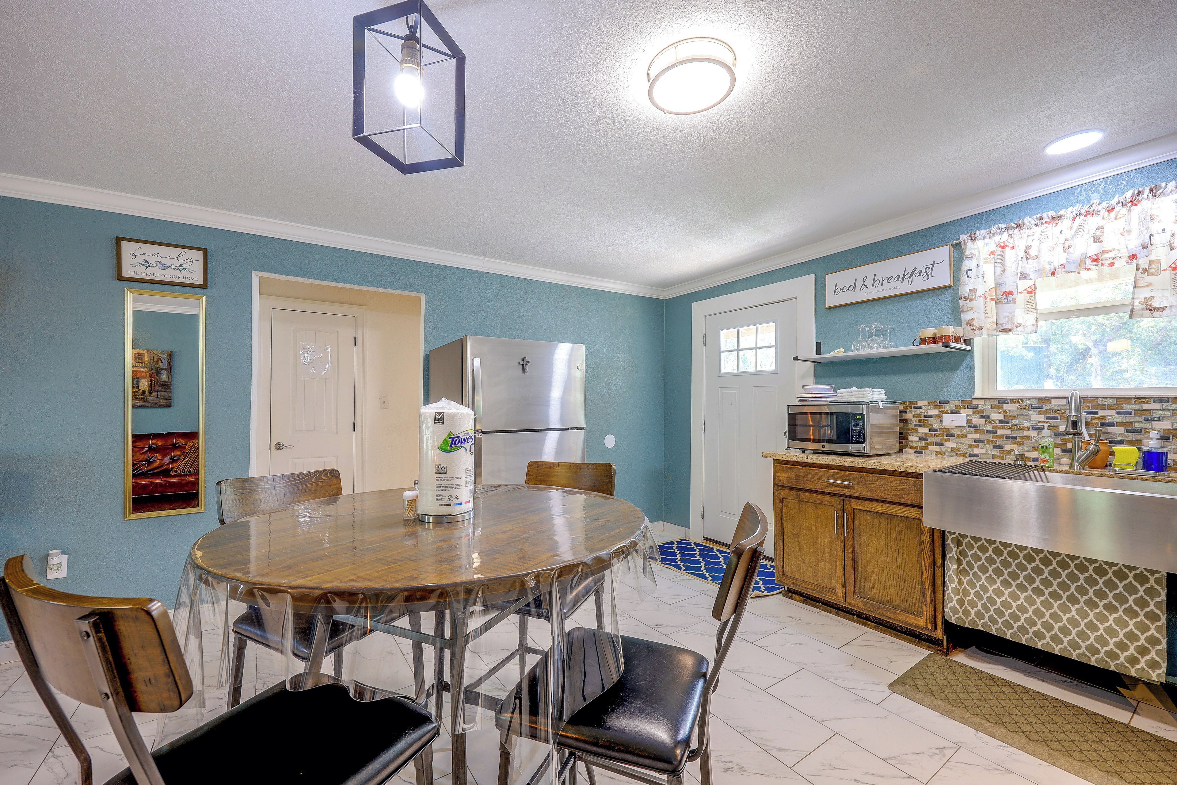 A kitchen with a dining table, chairs, a refrigerator, a microwave, and a window with curtains.