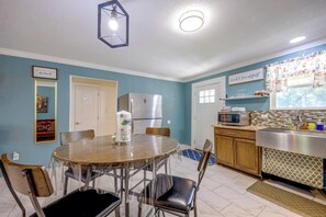 Una cocina con mesa, sillas, refrigerador, microondas y ventana con cortinas.