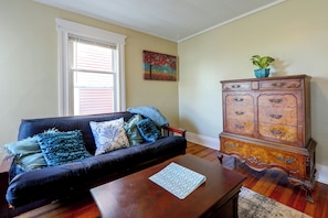A living room with a dark blue sofa, a wooden cabinet, and a window with blinds. - Walk to Rosamond Gifford Zoo & Dining! Cozy Unit (Syracuse)