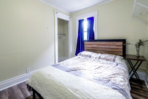 A bedroom with a bed, a nightstand, a window with curtains, and a door leading to another room. - Walk to Rosamond Gifford Zoo & Dining! Cozy Unit (Syracuse)