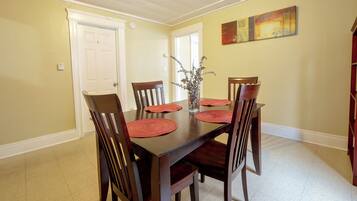 A dining room with a wooden table, six chairs, and a vase with dried flowers.