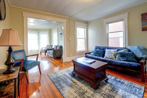 A living room with hardwood flooring, a blue sofa with patterned cushions, a wooden coffee table, and a lamp. - Walk to Rosamond Gifford Zoo & Dining! Cozy Unit (Syracuse)
