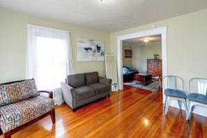 A living room with a sofa, a chair, a wooden cabinet, and a painting on the wall. - Walk to Rosamond Gifford Zoo & Dining! Cozy Unit (Syracuse)