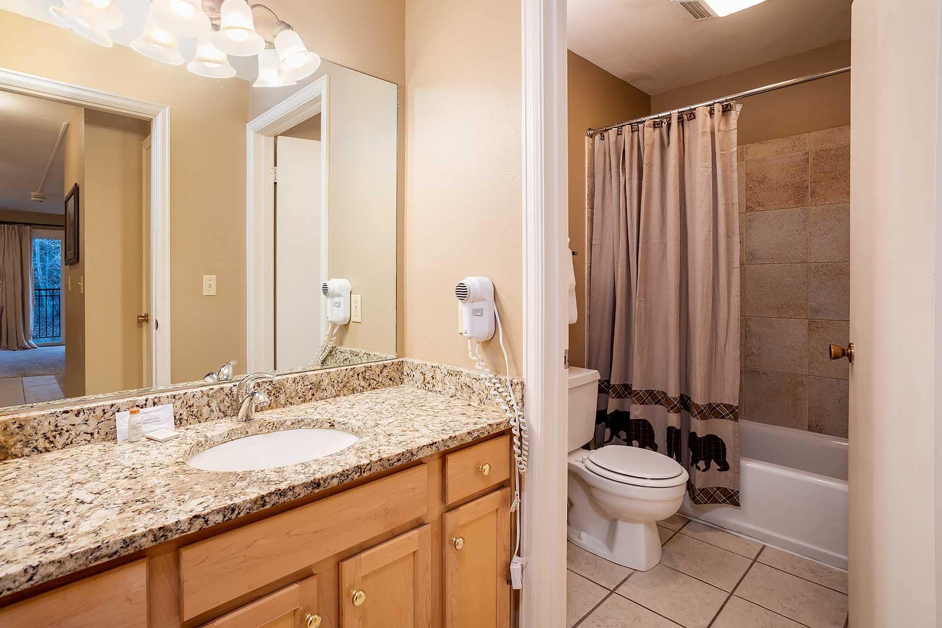 A bathroom with a granite countertop, two sinks, a toilet, and a shower with a curtain.