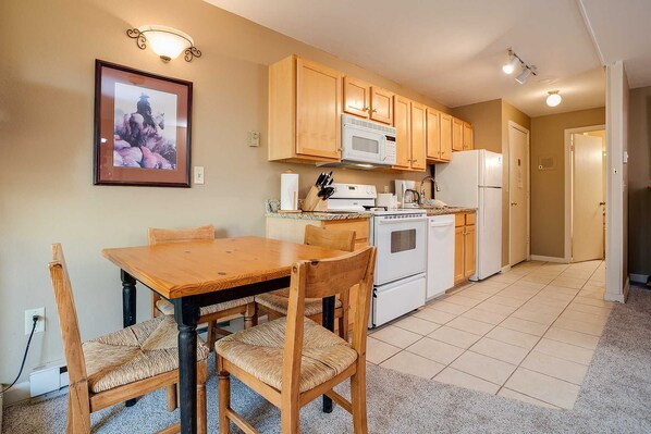 A kitchen with wooden cabinets, a microwave, a stove, and a refrigerator. There is a dining table with chairs. - Dreams in Steamboat Springs! Balcony, Heated Pool (Steamboat Springs)