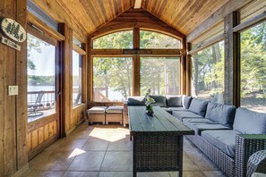 Uma cabana com interior de madeira, uma grande janela com vista para uma floresta e um sofá e mesa dentro.