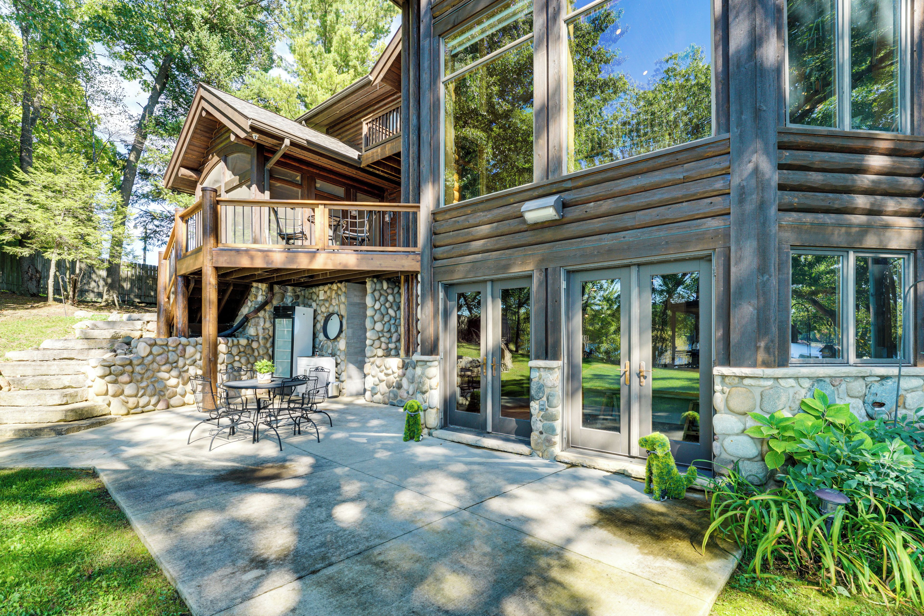 A two-story log cabin with a stone foundation, a balcony with outdoor furniture, and a stone wall.