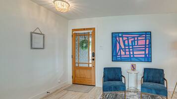 A room with a wooden door, a framed picture, two blue chairs, a small table, and a blue abstract painting on the wall.