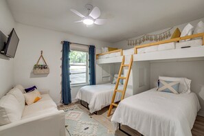 Una habitación con literas, ventilador de techo, ventana con cortinas, un pequeño sofá y un televisor montado en la pared.