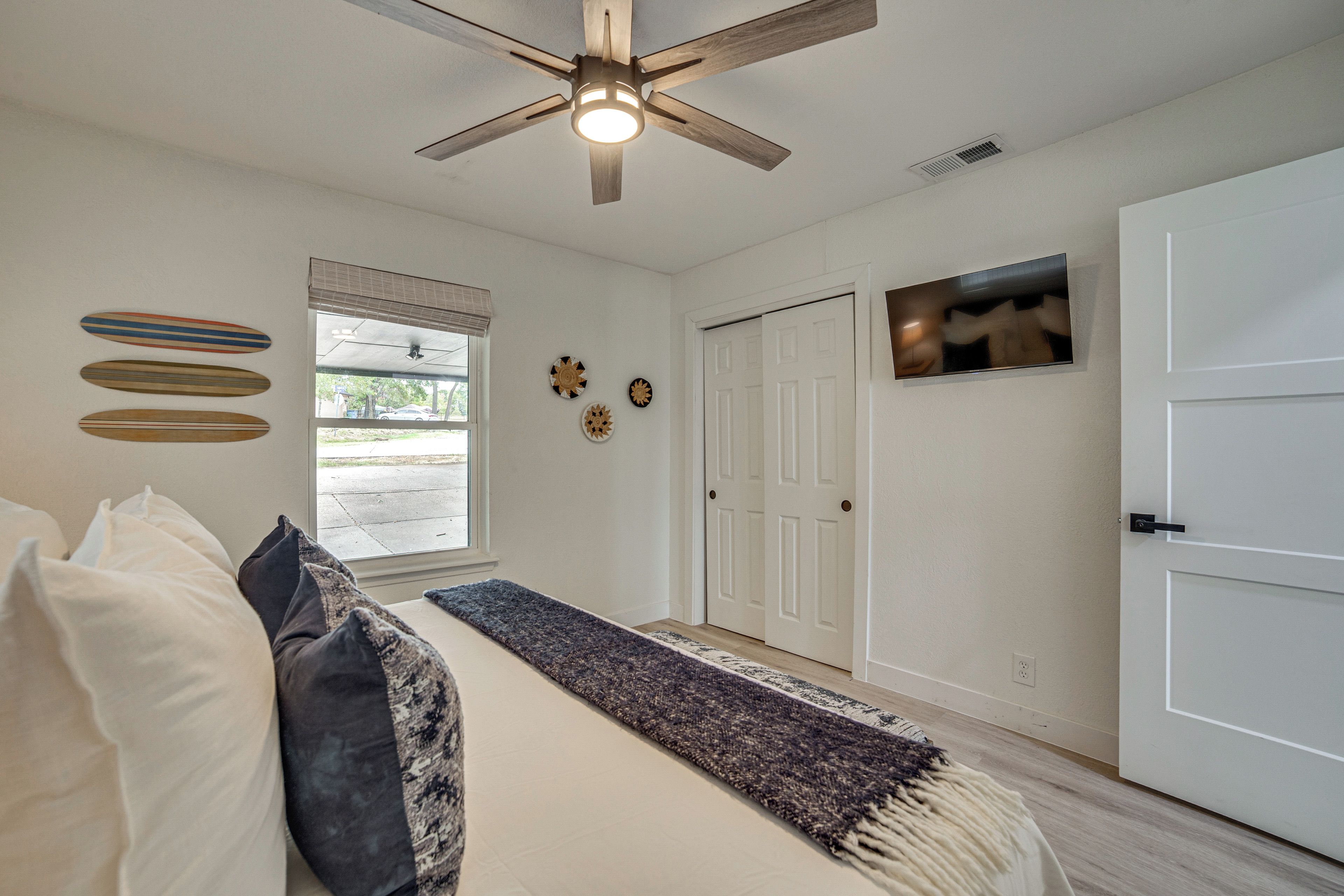 A bedroom with a bed, pillows, a ceiling fan, a window, and a door.