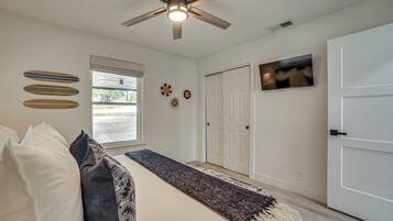 A bedroom with a bed, pillows, a ceiling fan, a window, and a door.