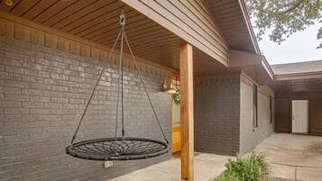 A hanging swing suspended from a wooden ceiling, a brick wall, and a door with a window.