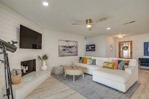 A modern living room with a white sofa, a fireplace, a mounted TV, and a ceiling fan. - Putt, Play & Splash! Cedar Creek Lake Getaway (Mabank)