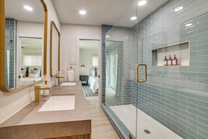 A modern bathroom with a glass shower enclosure, a vanity with a mirror, and a shelf with toiletries. - Putt, Play & Splash! Cedar Creek Lake Getaway (Mabank)