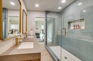 Un baño moderno con cabina de ducha de vidrio, tocador con espejo y repisa con artículos de aseo.