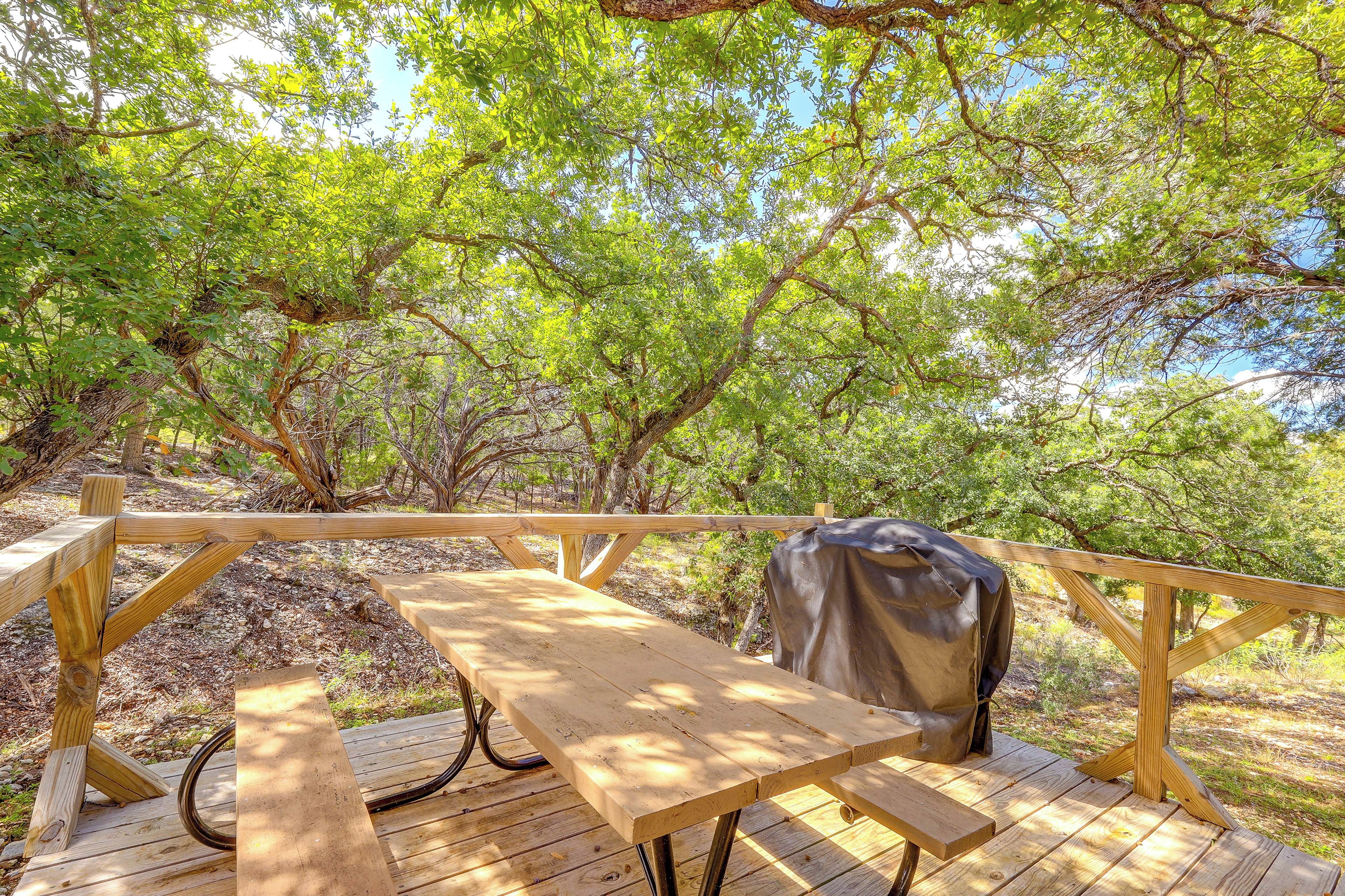 A wooden deck with picnic tables and a covered grill area, surrounded by trees.