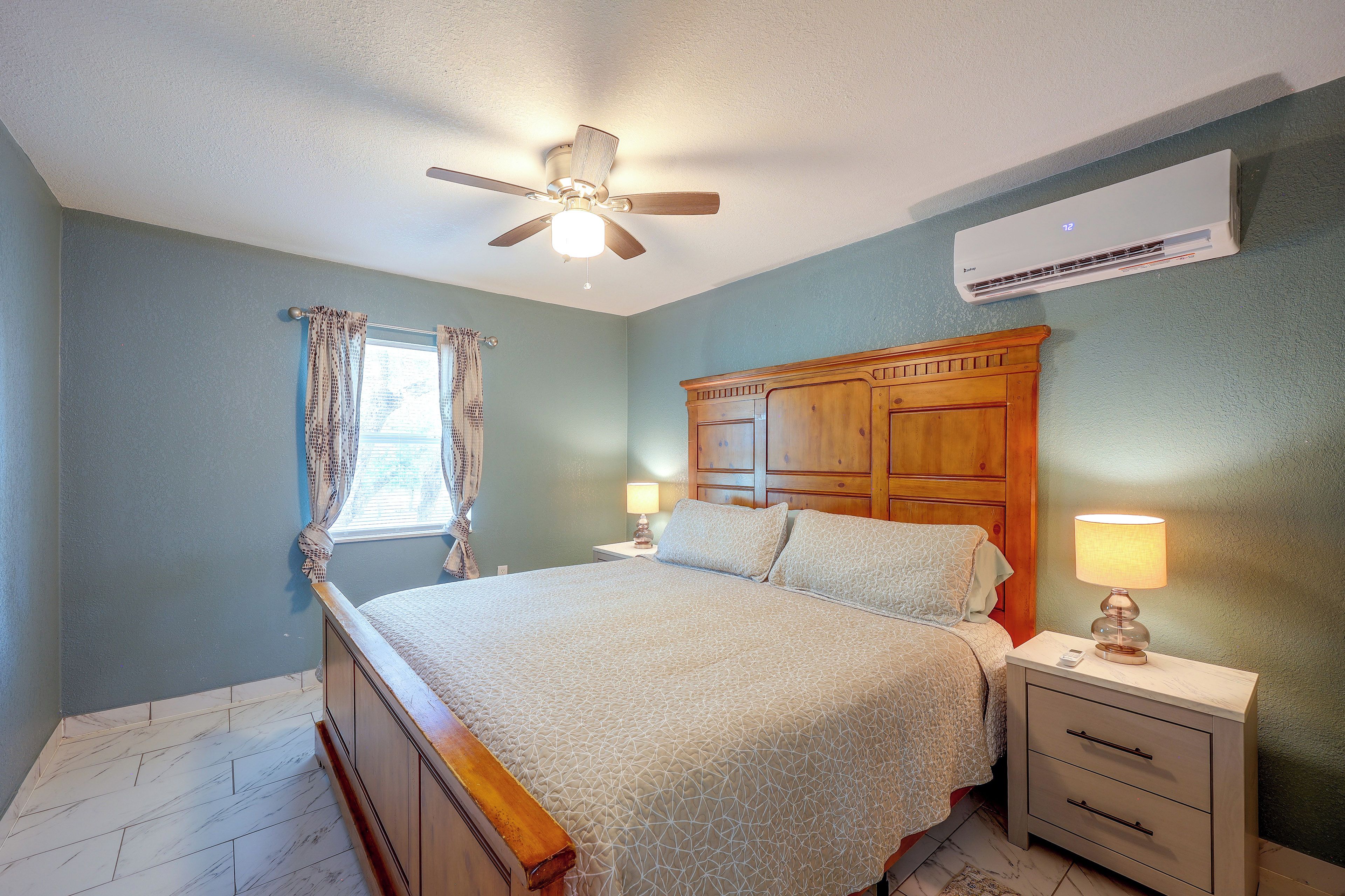 A bedroom with a bed, nightstands, a ceiling fan, and an air conditioning unit.