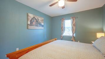 A bedroom with a bed, a ceiling fan, a window with curtains, and a wall painting.