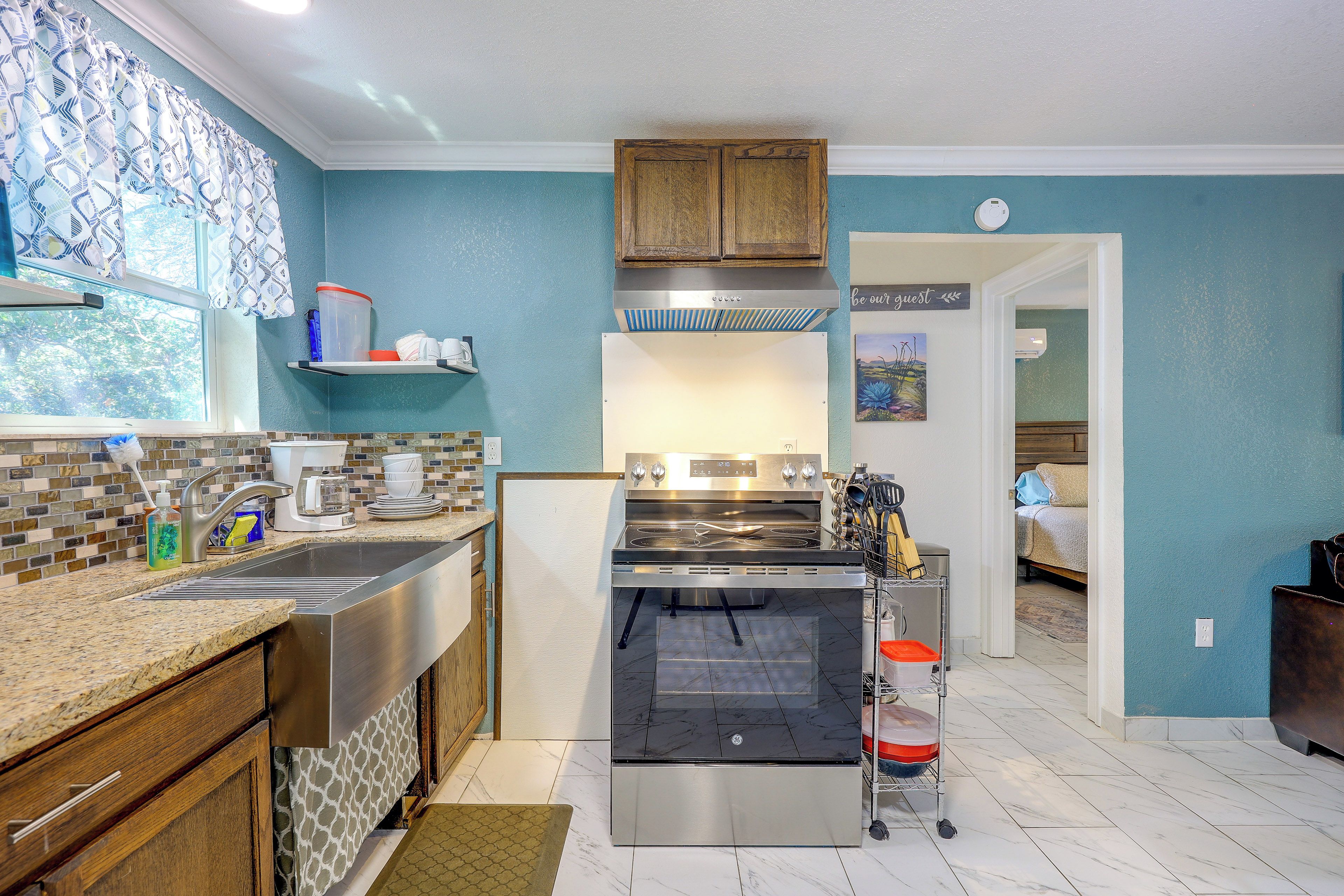 A modern kitchen with a stainless steel range, a built-in oven, and a window with patterned curtains.