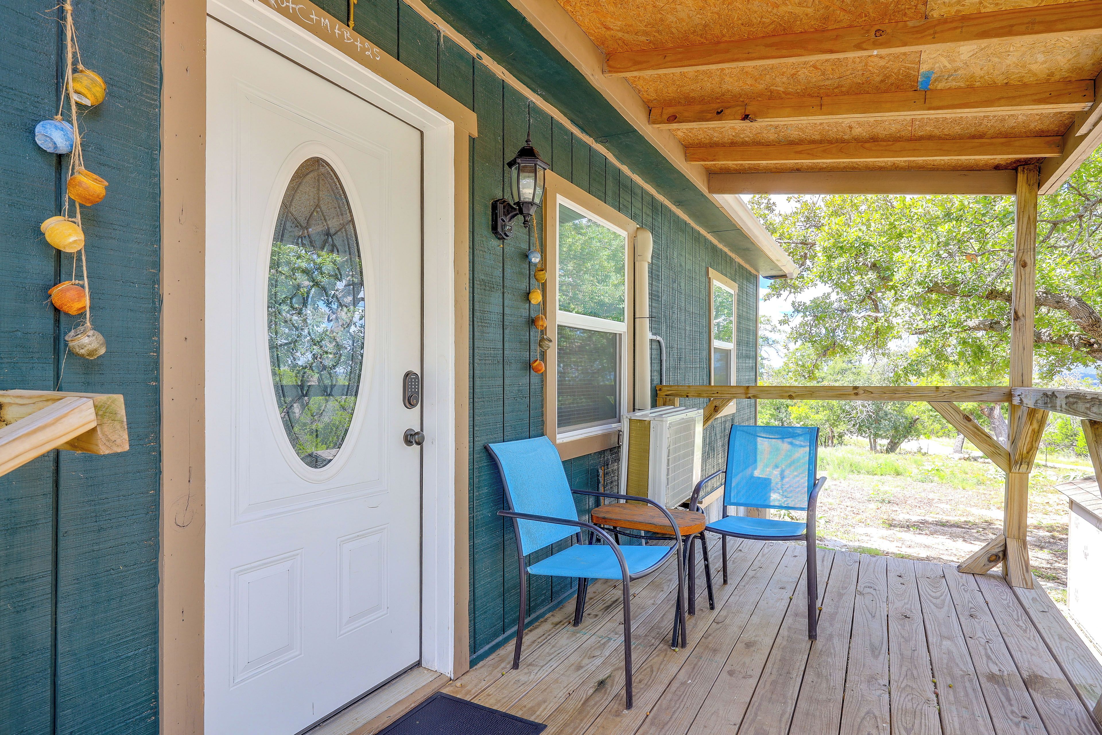 A wooden deck with two chairs, a white door with a window, and a porch railing.