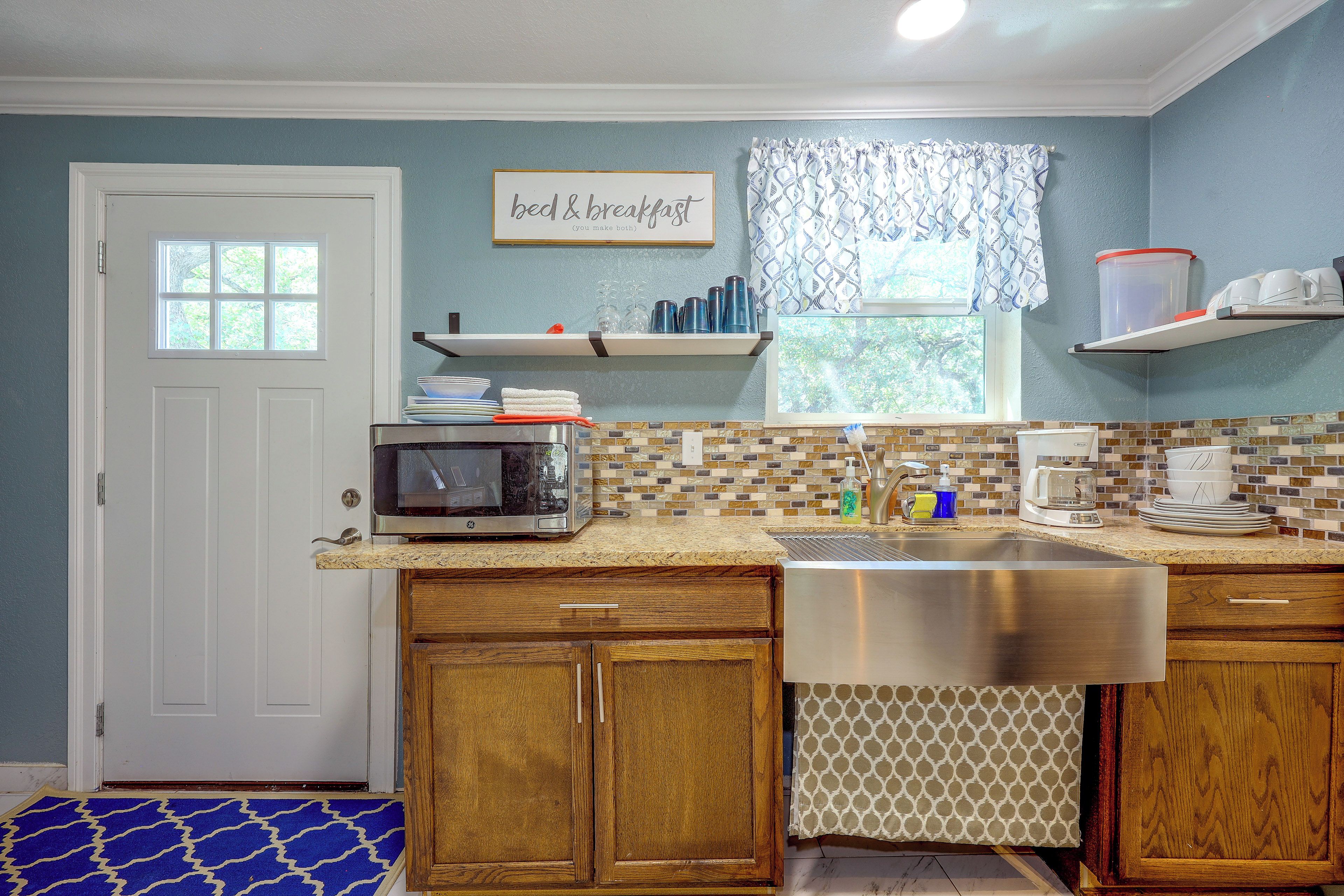 A kitchen with a microwave, sink, and a window with a view of trees.