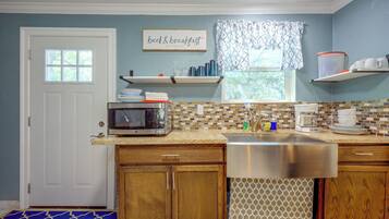 A kitchen with a microwave, sink, and a window with a view of trees.