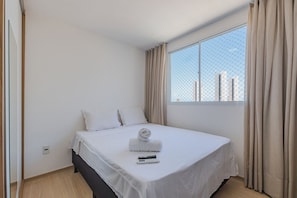 A hotel room with a single bed, a window with curtains, and a view of buildings outside. - Mirante #902 - Balcony With Sea View By Carpediem (Fortaleza)