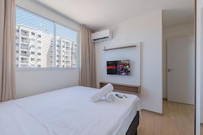 A hotel room with a bed, a TV mounted on the wall, and a window with a view of a building. - Mirante #902 - Balcony With Sea View By Carpediem (Fortaleza)