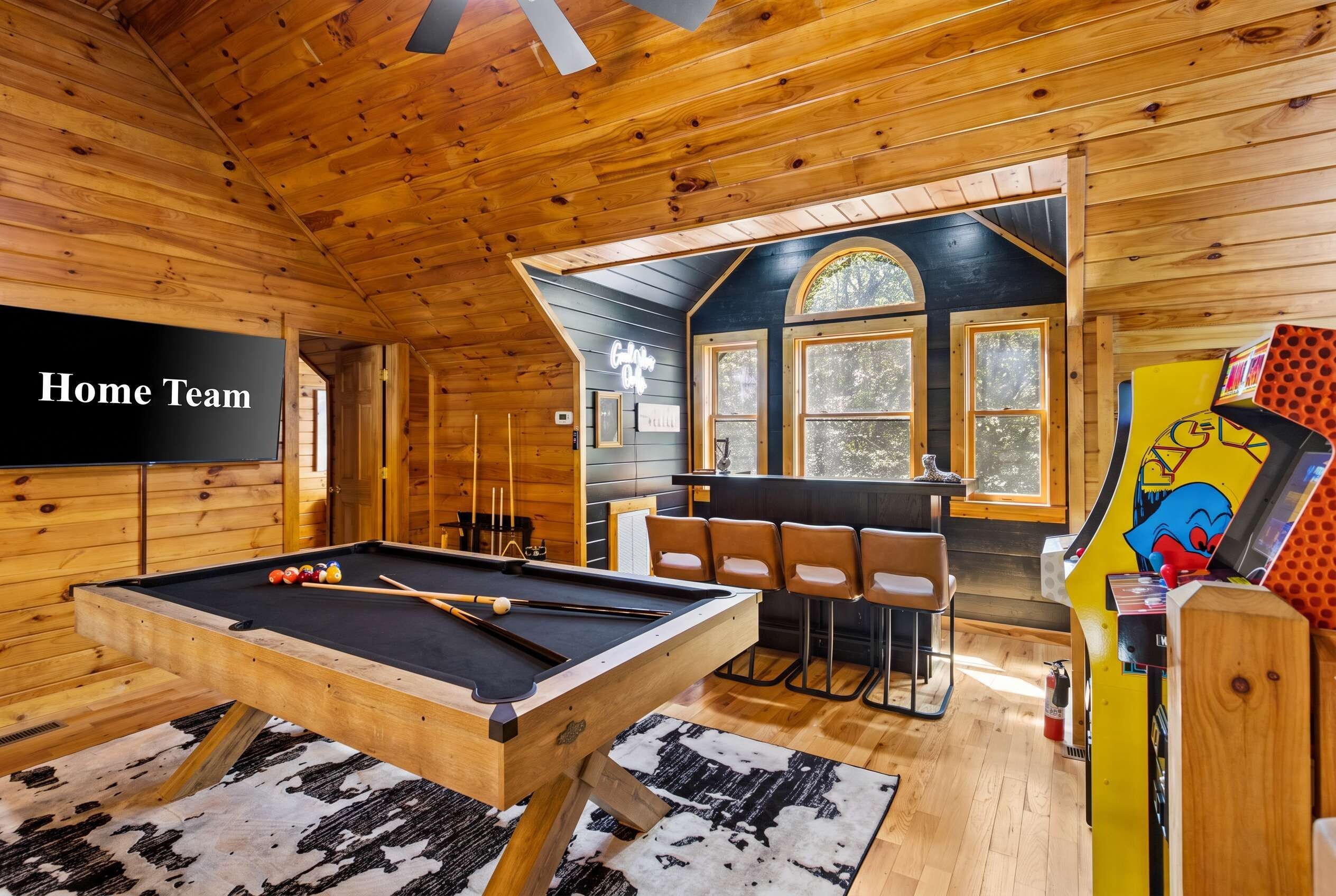 A wooden interior with a pool table, chairs, and a neon sign.