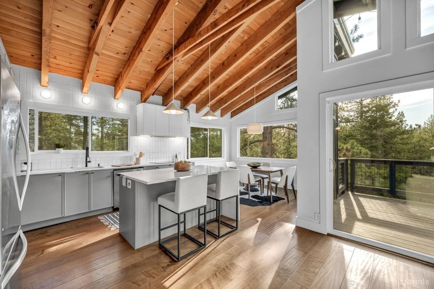 A modern kitchen with wooden beams, large windows, and a dining area with a view.