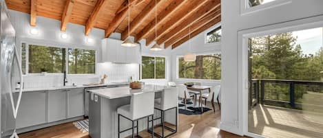 A modern kitchen with wooden beams, large windows, and a dining area with a view.