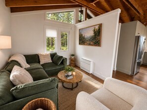 A cozy living room with a green sofa, a white armchair, a round coffee table, and a painting on the wall. - 3739 Terrace Drive 2 Bedroom Home (South Lake Tahoe)