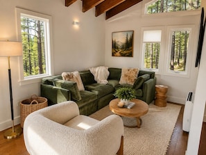 A cozy living room with a green sofa, a white armchair, a round wooden coffee table, and a painting of a forest on the wall. - 3739 Terrace Drive 2 Bedroom Home (South Lake Tahoe)