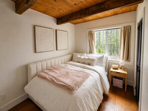 A bedroom with a large bed, a nightstand, a window with curtains, and two wall-mounted artworks. - 3739 Terrace Drive 2 Bedroom Home (South Lake Tahoe)