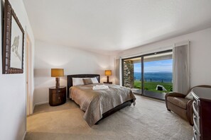 A hotel room with a large bed, two bedside lamps, a view of the sea, a stone wall, and a leather armchair. - 225 Beach Drive 4 Bedroom Home (South Lake Tahoe)