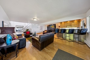 Ein geräumiger Wohnbereich mit einer Couch, Sesseln, einem Couchtisch und einer Küchenzeile mit Barhocker.
