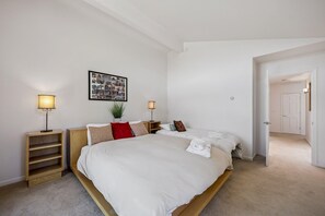 Ein Schlafzimmer mit einem großen Bett, zwei Nachttischen inklusive Lampen, einer Wandcollage und einer Tür zu einem anderen Raum.