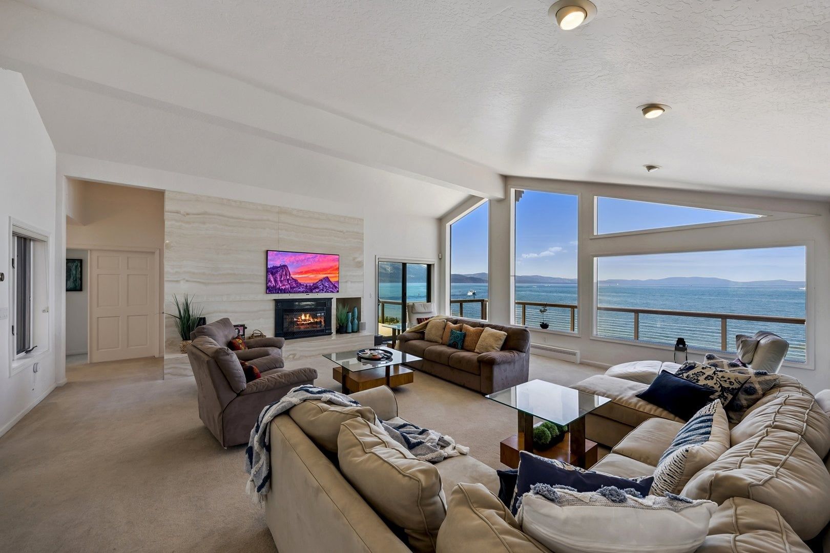 A spacious living room with a fireplace, large windows, and a view of the sea.