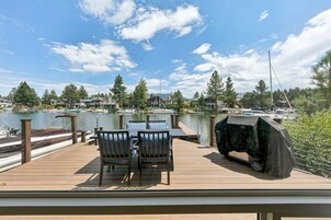 Um deck de madeira com mesa e cadeiras, com vista para uma marina e casas ao fundo.