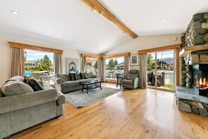 Ein geräumiges Wohnzimmer mit Kamin, einer Sofagarnitur und Blick auf Pool und Berge.