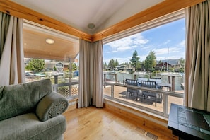 A cozy cabin room with a large window overlooking a dock and boats, a wooden deck, and a comfortable seating area. - 615 Alpine Drive 3 Bedroom Home (South Lake Tahoe)