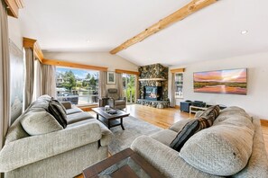 A spacious living room with a fireplace, comfortable seating, and a large window overlooking a scenic outdoor area. - 615 Alpine Drive 3 Bedroom Home (South Lake Tahoe)