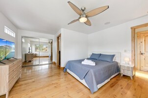 Un dormitorio con una cama, una mesita de noche, un ventilador de techo y un televisor sobre un aparador.