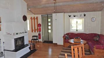 A living room with a fireplace, wooden ceiling, a red sofa, and a dining table.